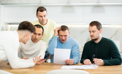 Friends reading financial documents and trying to solve problems together while sitting at table in their home kitchen