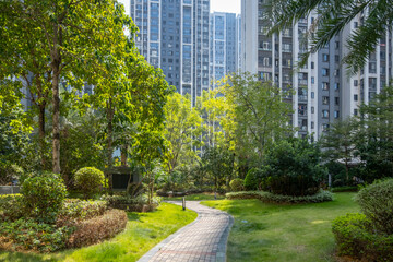 A well-maintained park with a paved walkway winding through trees and shrubs. A natural environment in a communal garden of some high-rise residential apartment building blocks in urban neighbourhood