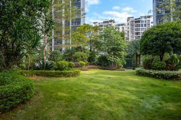 Contemporary residential landscape featuring trees and grass lawn in manicured gardens, surrounded by modern high-rise apartments. A communal public outdoor space in a  populated Chinese neighborhood