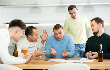 Fototapeta premium Man appearing upset as reading document, while friends gathering around, offering support and advices during friendly meeting at home kitchen..