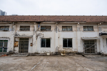 A dilapidated, desolate, abandoned factory warehouse building shows signs of neglect, featuring peeling paint, broken windows, and a grimy exterior