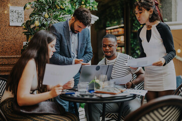 Multiracial group of business professionals collaborating and strategizing in a modern coffee bar. They are engaged in discussion, sharing ideas and reviewing documents for a project.