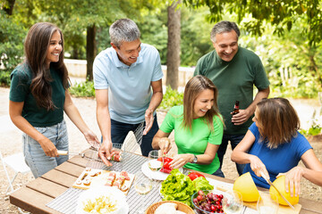 A lively group of friends shares laughter and delicious food while grilling in a green park. They prepare fresh vegetables and enjoy refreshing drinks in the sunny atmosphere.