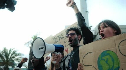 Man shouting with megaphone at protest against pollution of planet in community. Group diverse people complaining with raised fist in demonstration against global warming with climate change banners