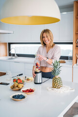 Smiling Woman Blending Fruits for a Smoothie in Organized Kitchen