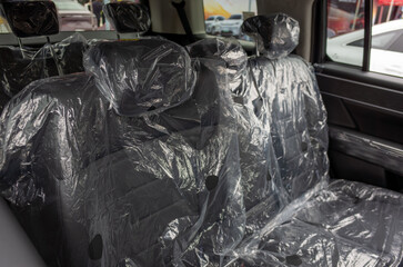 The interior of a brand-new car with new and unused black leather seats covered in plastic protective covers. Transparent wrapping covers the car seats.