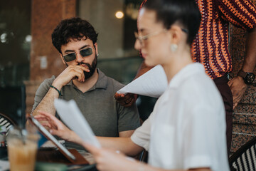 Focused team having a business meeting in a coffee shop, discussing documents and working together on a laptop.