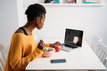 A woman is maintaining focus on work while enjoying a nutritious salad at her home workspace