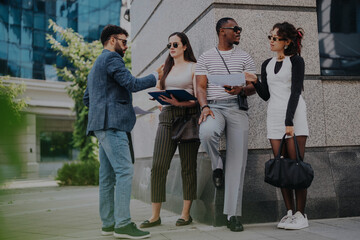 Fototapeta premium A group of young professionals casually discuss business outdoors. They are dressed smartly and appear engaged in conversation, highlighting teamwork and collaboration in a corporate environment.