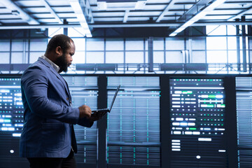African american man in data center monitoring system performance, identifying bottlenecks and...