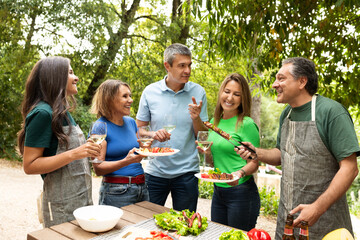 Friends celebrate together at a barbecue, sharing laughter and delicious food in a verdant garden. The sun shines as they toast with drinks and savor the moment.