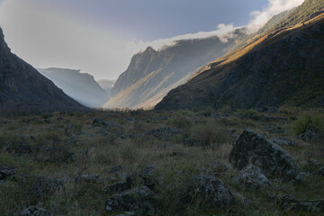 Panoramic landscape of a mountain valley the bottom. Rocky slopes from the both sides. Peaks in th morning sunlight. Ground is a grass meadow with rocks. September in Altai: golden autumn nature.