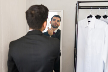 Man in business attire is applying cologne while checking his reflection in the walk-in closet mirror