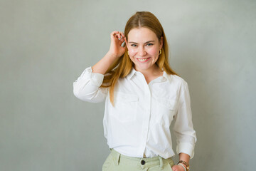 Flirty young woman with long hair is posing in a studio, touching her hair and smiling