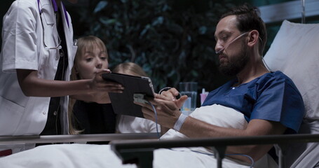 Happy family young man with oxygen tube in nose mother and daughter sit near lovely husband man signs agreement for surgery.