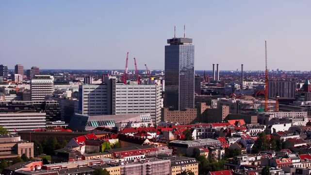 Urban sprawl rapidly expands in Berlin, showcasing an aerial view filled with construction cranes and towering skyscrapers including Park Inn by Radisson across the cityscape