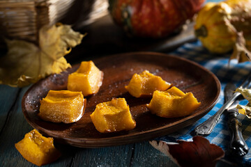 Pieces of baked pumpkin in a wooden plate on a blue wooden table