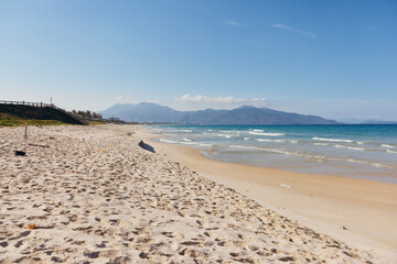 Beautiful Sandy Beach with Footprints, Majestic Mountain, and Clear Blue Sky on a Sunny Day