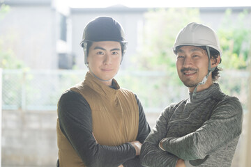 作業着を着たガテン系で働くヘルメットを被る二人のカメラ目線の笑顔