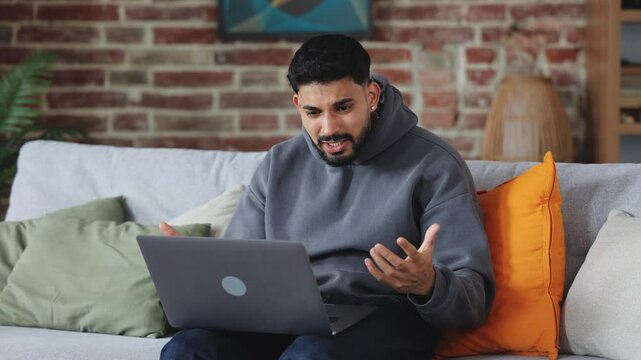Irritated man in casual clothes yelling in despair during video call through portable computer and throwing gadget aside. Frustrated person laying on couch and trying calming down after stress.