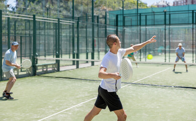 Obraz premium Adult man and young man doubles playing against two men in padel tennis on court