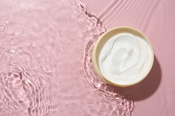 Cosmetic product. Jar with cream in water on pink background, top view. Space for text