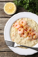 Delicious risotto with shrimps, cheese, lemon and parsley on wooden table, top view