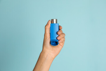 Woman holding asthma inhaler on light blue background, closeup