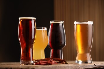 Glasses with different types of beer and snacks on wooden table against color background