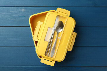 Yellow lunch box with cutlery on blue wooden table, top view