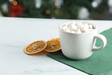 Tasty hot cocoa drink with marshmallows in cup and dry orange slices on white table, closeup. Space for text