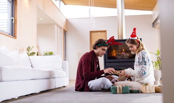 Christmas time, exchanging gifts by fireplace, couple wearing festive hats in cozy moment, at home