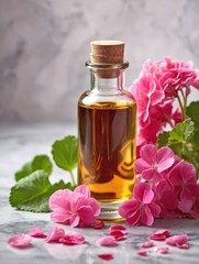 A small glass bottle of geranium oil rests on a smooth marble surface, surrounded by scattered pink geranium petals and a few whole flowers in full bloom.