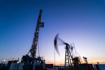 Obraz premium in the evening, oil pumps are running, The oil pump and the beautiful sunset reflected in the water, the silhouette of the beam pumping unit in the evening.