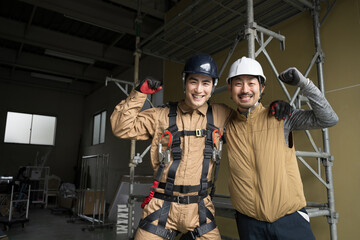  Two workers working in steeplechase and outdoor safety belt harnesses and air-conditioning suits, looking at the camera, smiling, and posing with good-natured gusto.