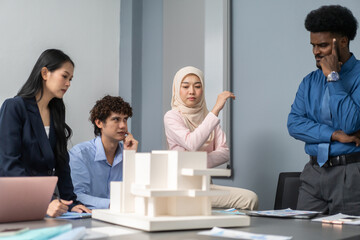 Architects engineers collaborating on building design project in modern office, diverse team of professionals female muslim architect and male engineers discussing architectural model of structure