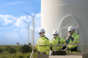 Fototapeta premium engineers stand on a platform, equipped with safety gear and ropes, in front of a wind farm. Wind turbines stretch across the background, showcasing the renewable energy infrastructure.