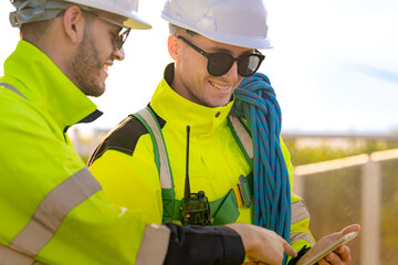 Two engineers in safety helmets and high visibility jackets engage in a field inspection. One is...