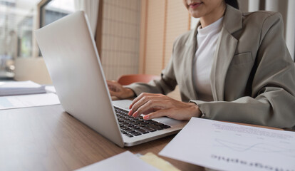 Professional Business Woman Sitting at Desk and Reviewing Work Documents on Laptop in Modern Office Setting