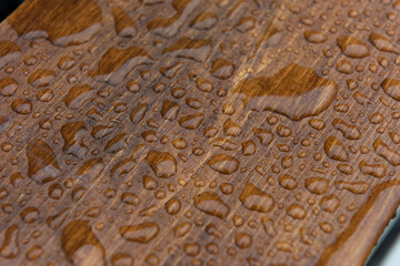 Close up of a stained and sealed waterproof wooden board covered in water drops