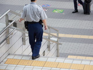 昼の都市の繁華街で巡査している男性警備員の姿