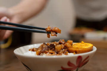 Chopsticks lifting braised pork above a bowl of braised pork rice.