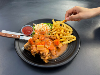Woman's hand pick a French fried from a Hainanese chicken chop plate served with salad.