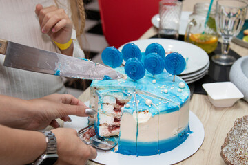 A birthday cake decorated with round blue lollipops and blue topping. Mom and child cutting the cake together on their birthday.