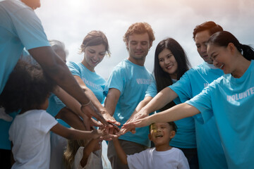 A group of people are holding hands in a circle, with some wearing blue shirts that say "volunteers". Scene is positive and friendly, as the group appears to be enjoying each other's company