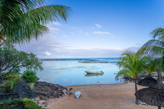 A small boat anchored in a calm turquoise lagoon, surrounded by a pristine white sandy beach and palm trees. The idyllic scene is captured at Ile aux Cerfs, Mauritius. Mauritius, Africa.