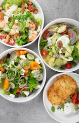 Three different vegetable salads and slavic draniki (potato pancakes) on gray marble background