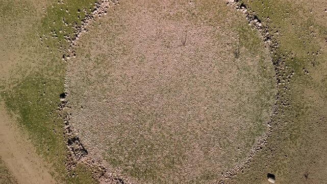 Drone perspective of a large cobbled threshing floor, traditionally used for agricultural tasks, located near vibrant waters in ruins from reservoir construction