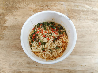 instant cup noodle with vegetables on isolated wooden background