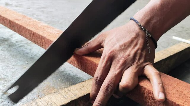 A man cuts wood with a handsaw, Man sawing wood into shape,Hand sawing a wooden block with a hacksaw